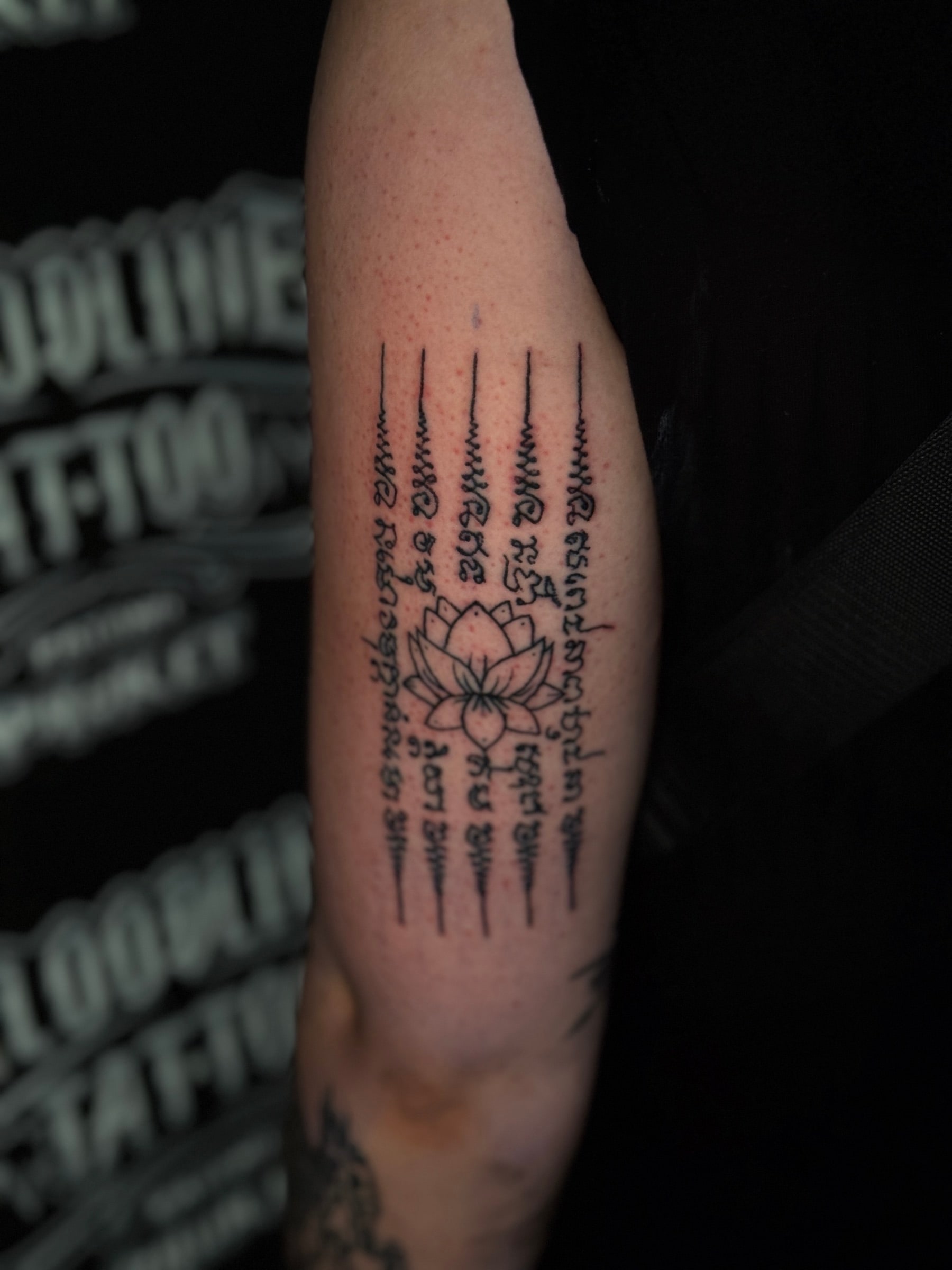 Hah Taew (Five Lines) Sak Yant with five vertical Khom script columns and unalome flourishes framing a central blooming lotus on the upper arm at Bloodline Tattoo Phuket.