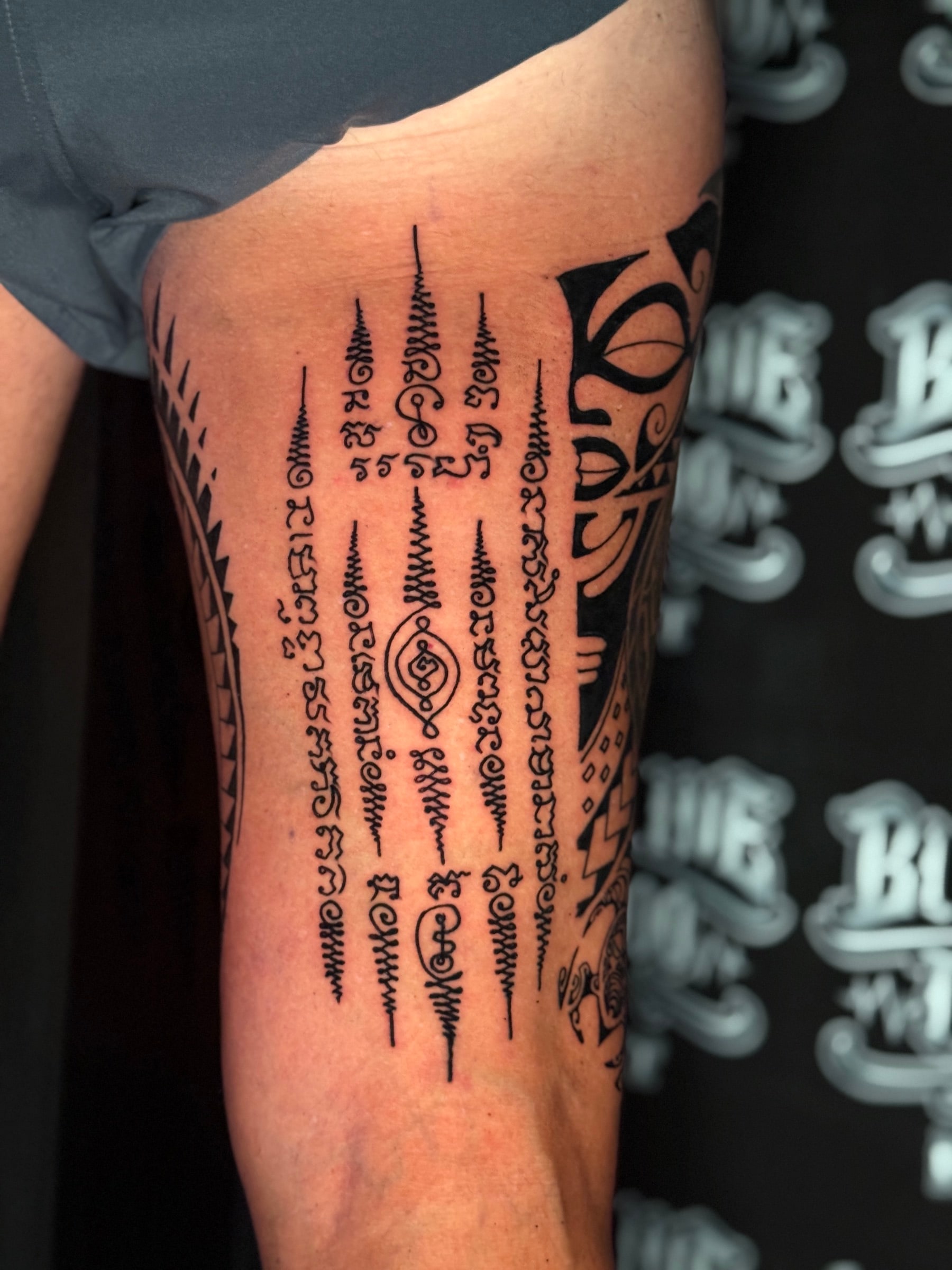 Hah Taew (Five Lines) Sak Yant with five vertical Khom script rows, unalomes, and a central diamond eye motif on the upper thigh at Bloodline Tattoo Phuket.