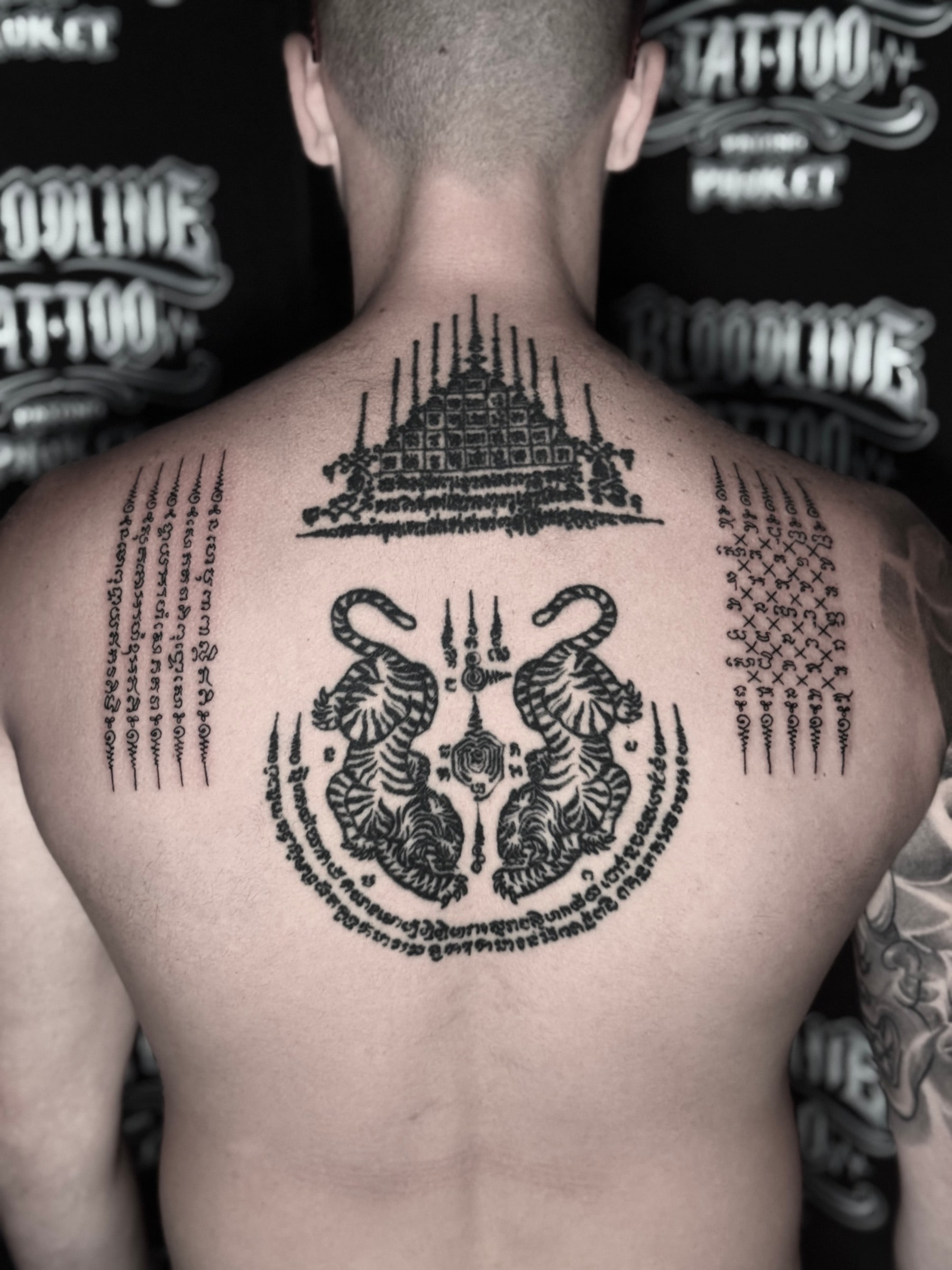 Full upper-back Sak Yant layout with Gao Yord nine spires, Suea Koo twin tigers, Hah Taew five lines, and geometric script yantras at Bloodline Tattoo Phuket.