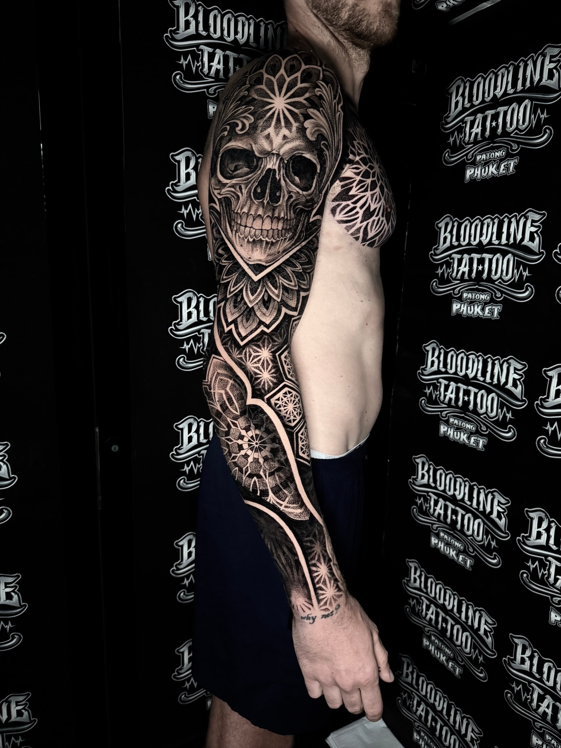 Blackwork mandala sleeve with a realistic skull bearing a forehead mandala, chest filigree, and star geometric wrist patterns at Bloodline Tattoo Phuket.