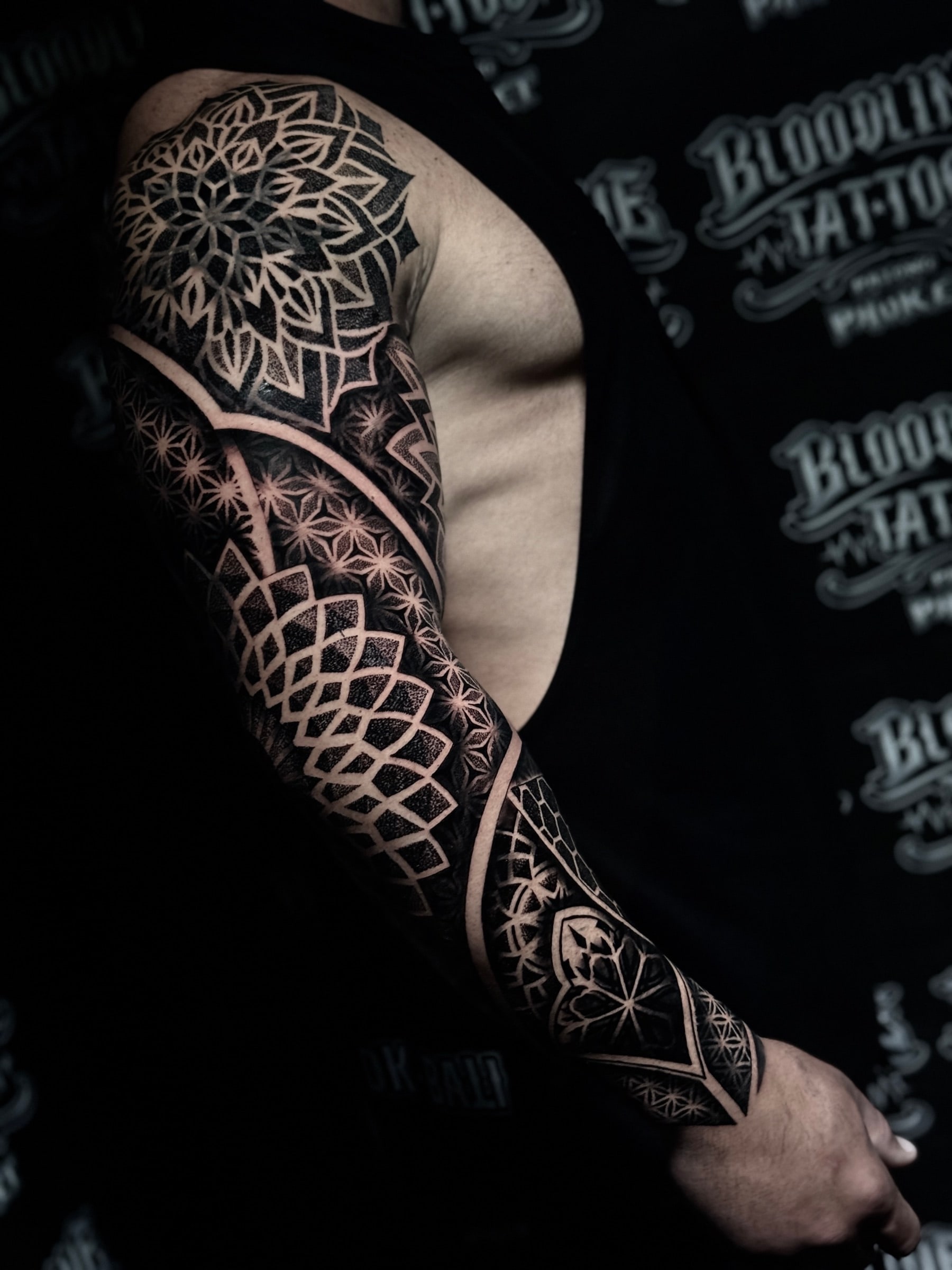 Dotwork mandala sleeve with a pointed shoulder mandala, Flower of Life mid-arm panels, and interlocking diamond forearm geometry at Bloodline Tattoo Phuket.
